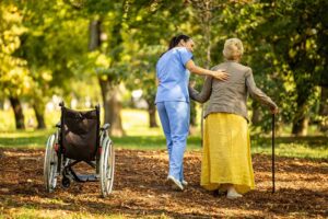 A senior resident sits with two family members, holding hands and sharing conversation in a cozy common room.