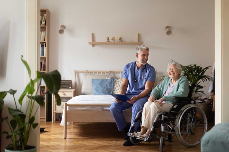 A nurse assists an elderly resident with organizing daily medication at a small dining table.