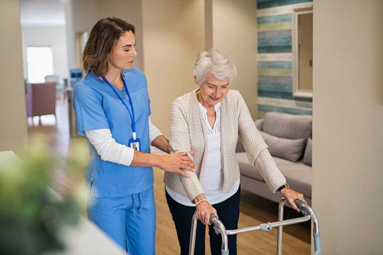 Two older adults laughing while doing gentle stretching together in a bright community room.
